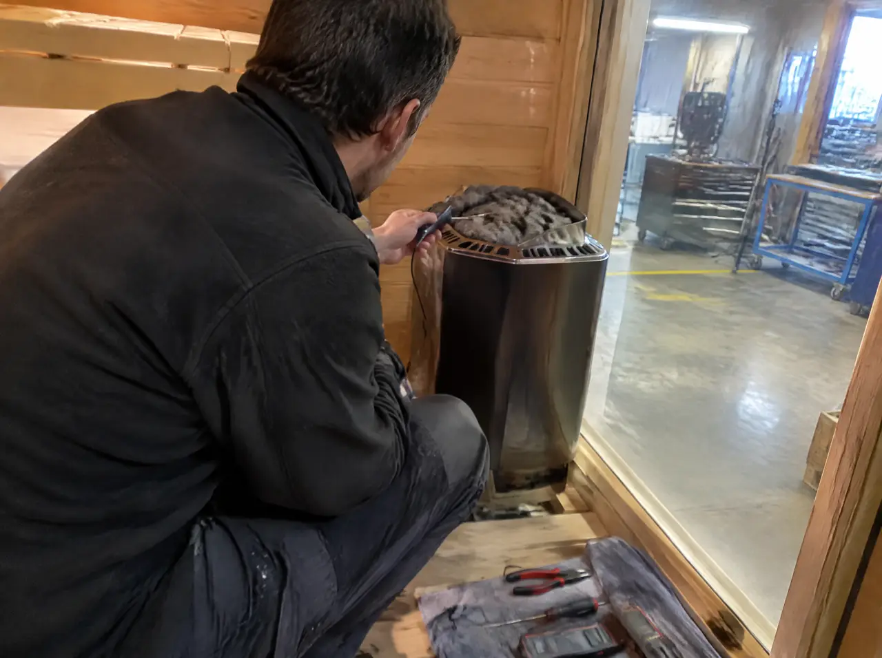 Technician checking a sauna heater in a cabin under test with a probe thermometer